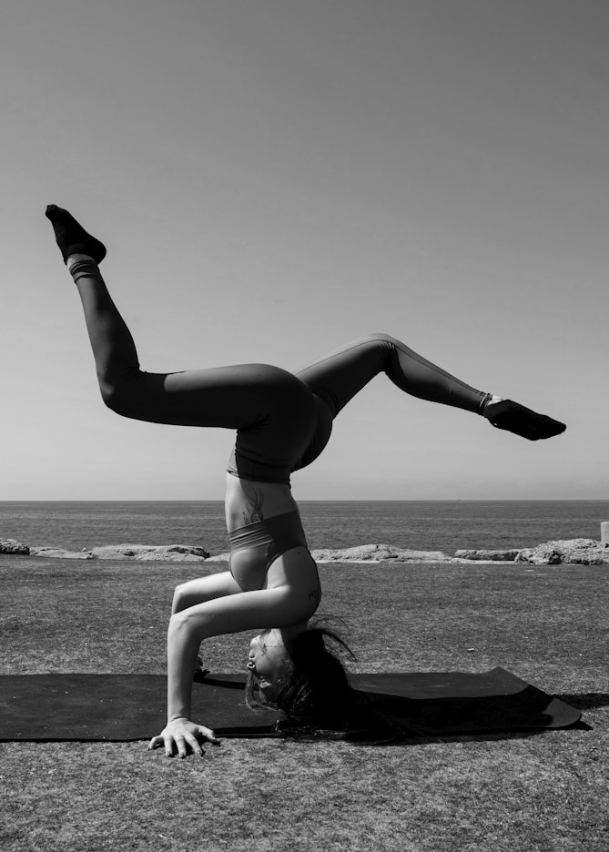 woman in black sports bra and panty bending on rock near sea