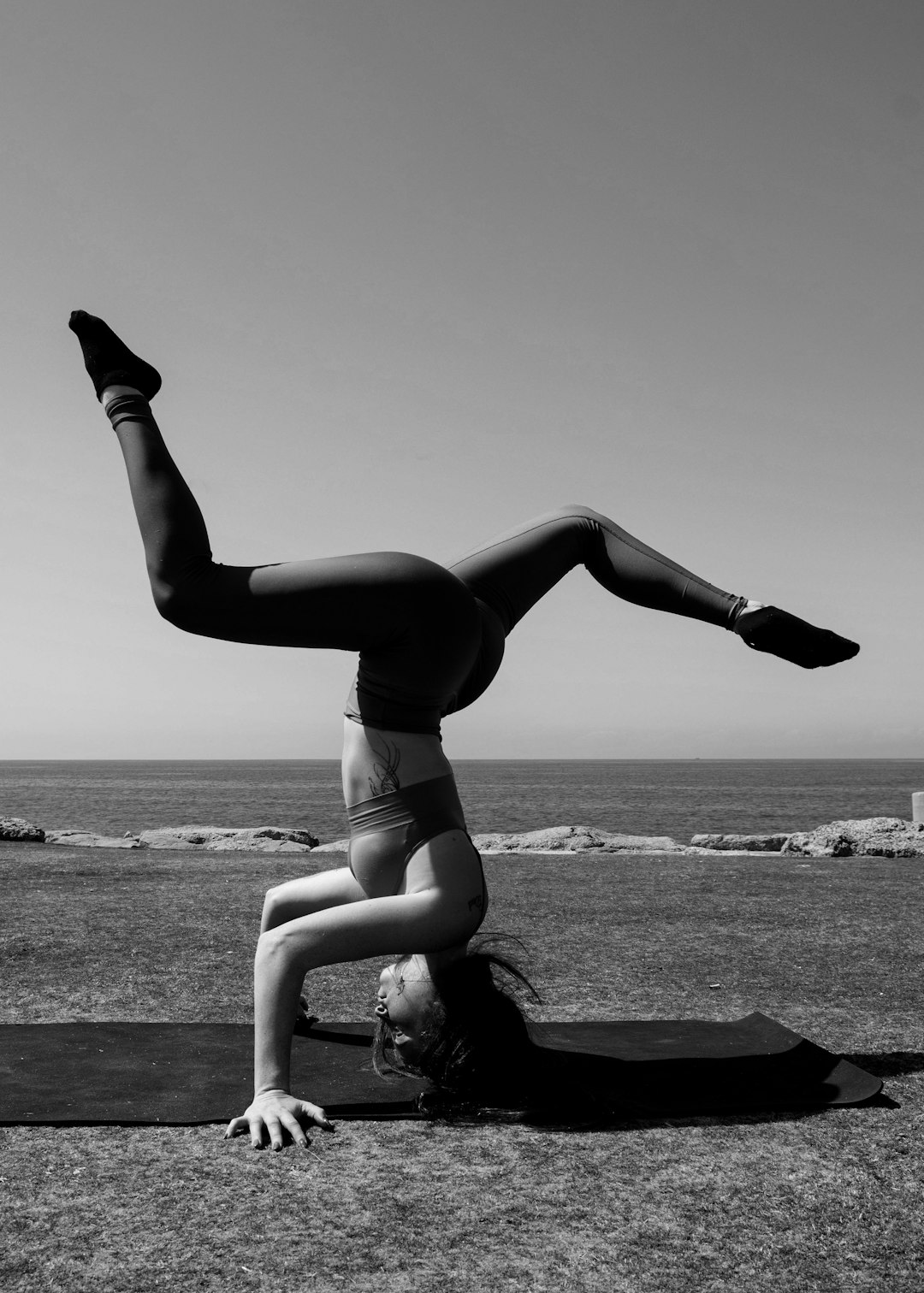woman in black sports bra and panty bending on rock near sea