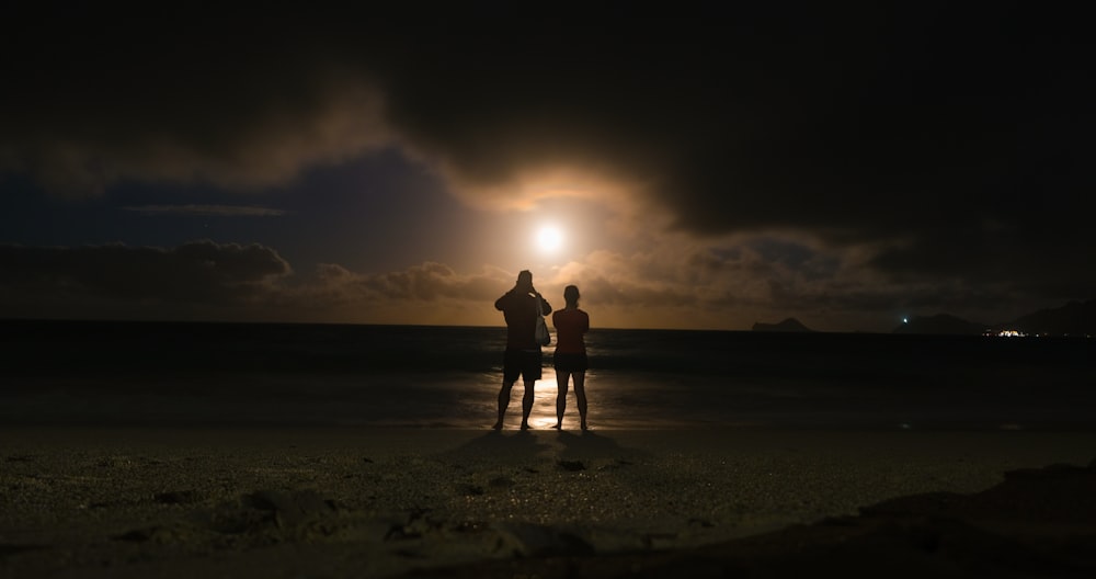 Silhouette von 2 Personen, die während des Sonnenuntergangs am Strand spazieren gehen