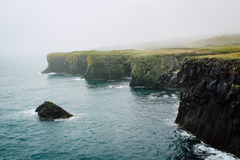 brown and green cliff beside body of water during daytime