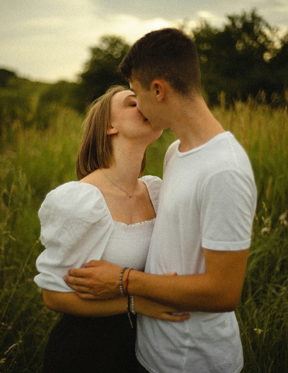 man in white shirt kissing woman in white shirt on green grass field during daytime