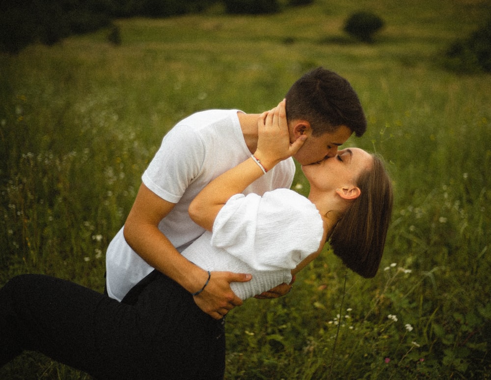 흰색 티셔츠를 입은 남자가 낮 동안 푸른 잔디밭에서 흰 셔츠를 입은 여자에게 키스