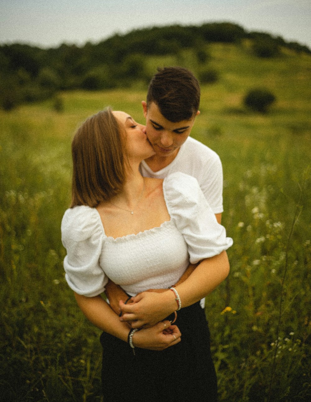 woman in white long sleeve shirt kissing man in black shirt on green grass field during