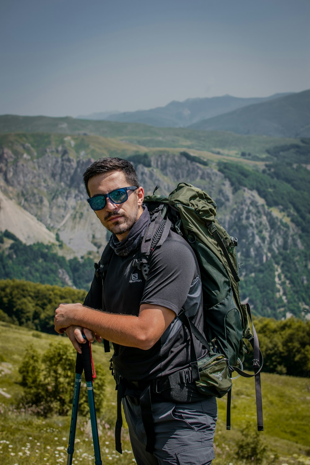 man in black t-shirt wearing black sunglasses and backpack standing on mountain during daytime