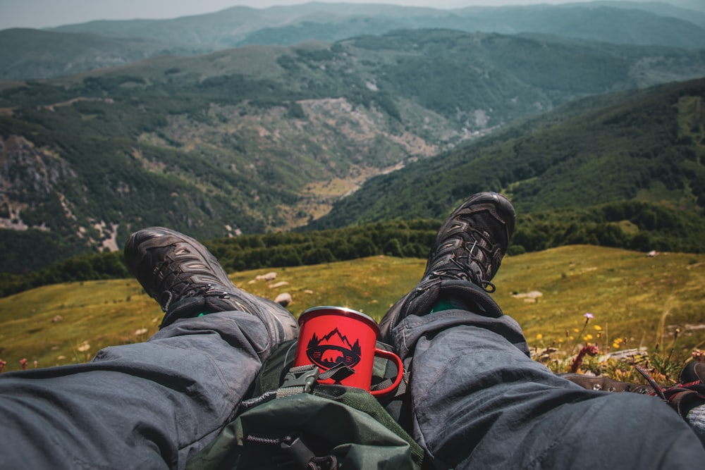 person in black pants and black hiking shoes sitting on rock mountain during daytime