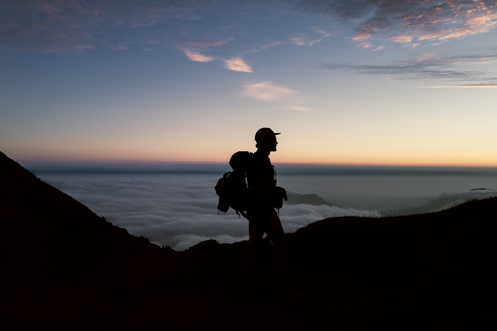 silhouette of man sitting on rock during sunset