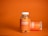 A clear plastic bottle with a white cap contains orange-colored gummies labeled as Jellybee Turmeric & Ginger. The bottle stands on an orange surface against an orange background. Next to it, another bottle lies horizontally, showing a similar label.