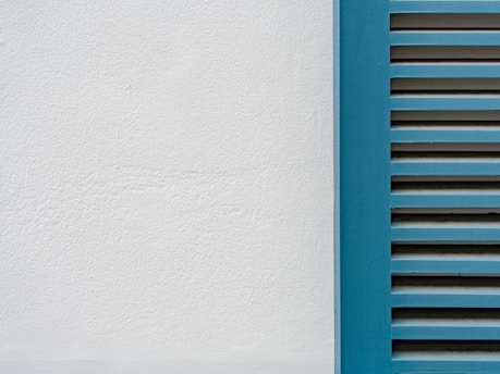 A minimalistic image featuring a close-up of a white plaster wall and a section of blue window shutters with horizontal slats.