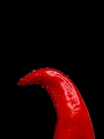 A vibrant red chili pepper with water droplets on its surface is set against a stark black background, creating a dramatic contrast.