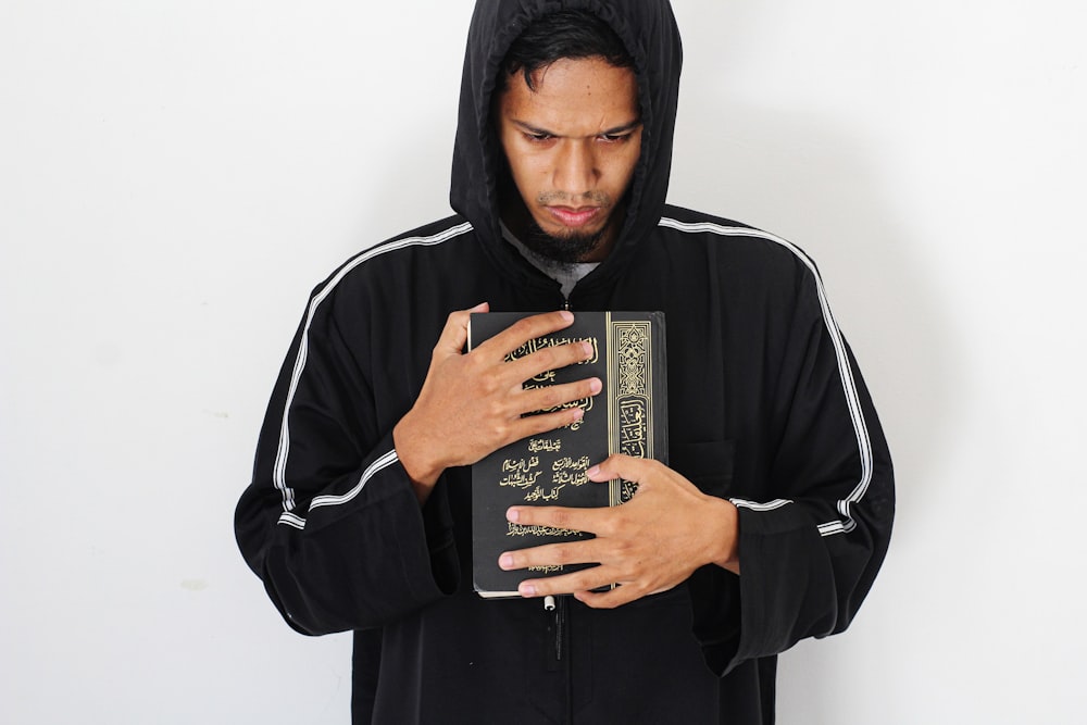 man in black and white hoodie holding black and white book