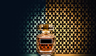 Close-up of a beautifully designed attar bottle resting on rich dark wood with golden Arabian patterns softly glowing in the background.