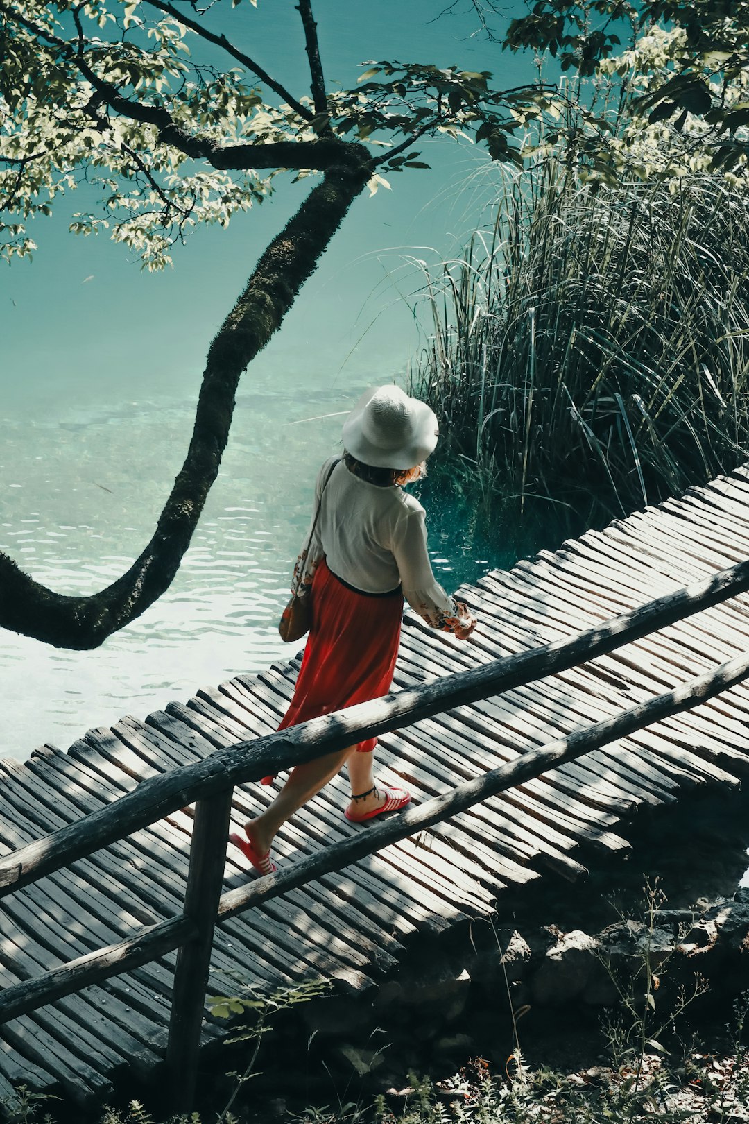 woman in white tank top and orange skirt walking on wooden bridge during daytime