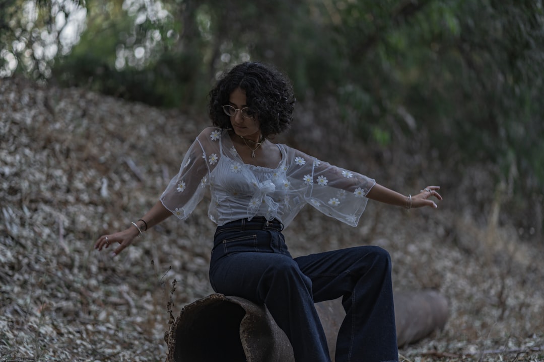 woman in white long sleeve shirt and blue denim jeans sitting on rock during daytime