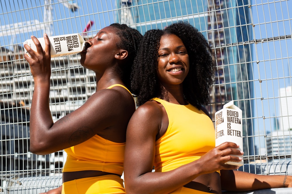 2 women in yellow tank top holding white and yellow labeled box
