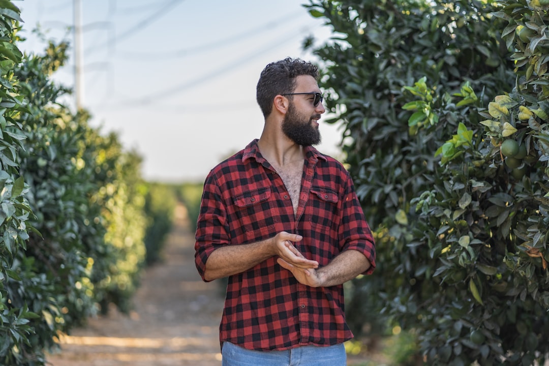 man in red and blue plaid button up shirt standing near green plants during daytime
