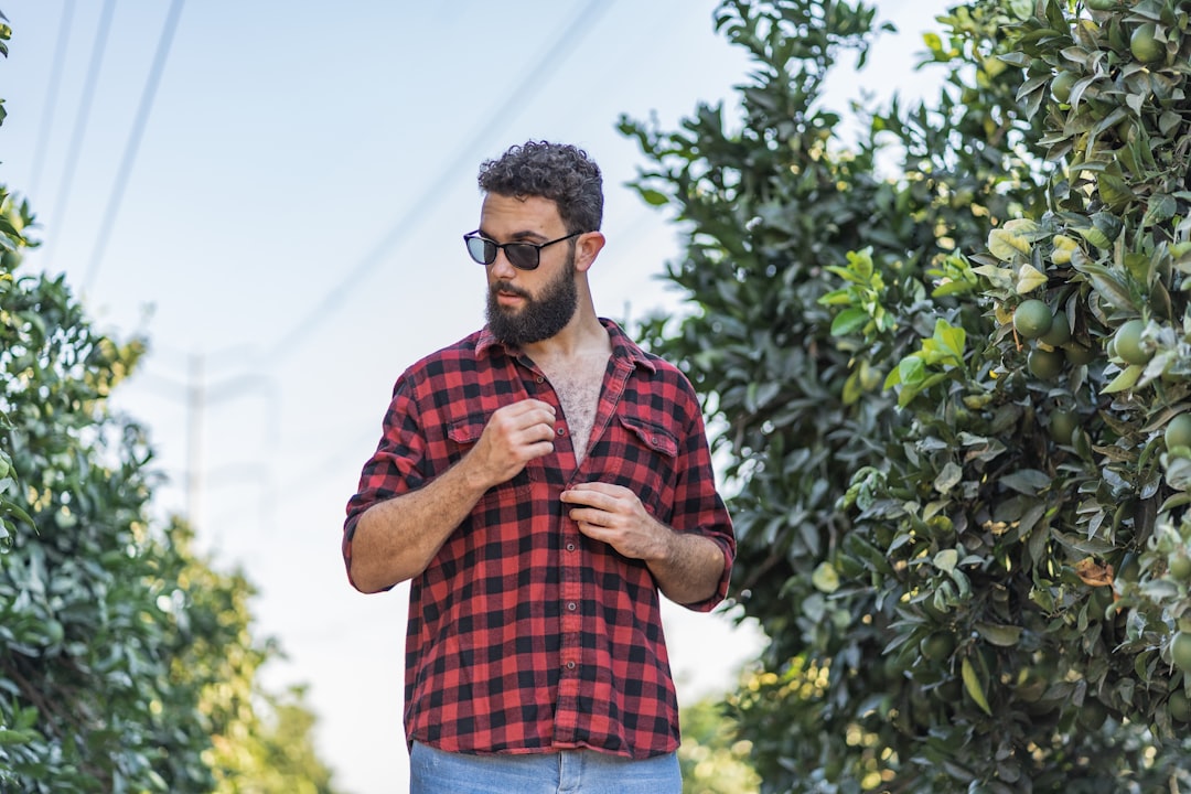 man in red and blue plaid button up shirt wearing black sunglasses standing near green leaf