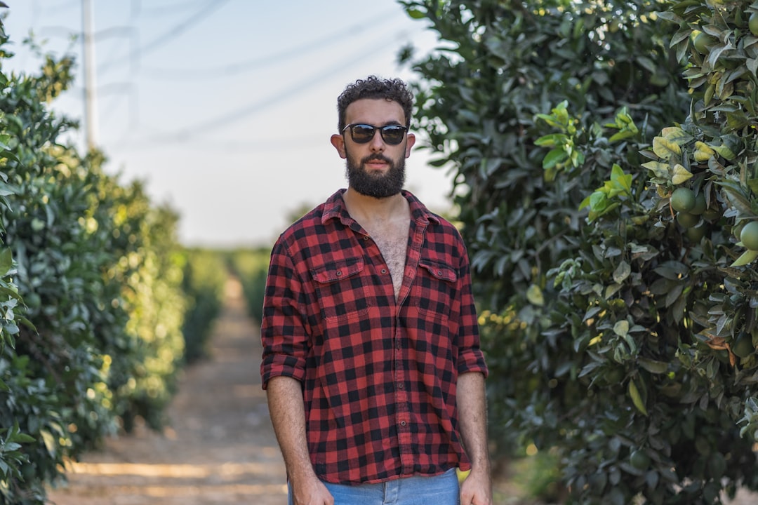 man in red and black plaid button up shirt wearing black sunglasses standing near green plants