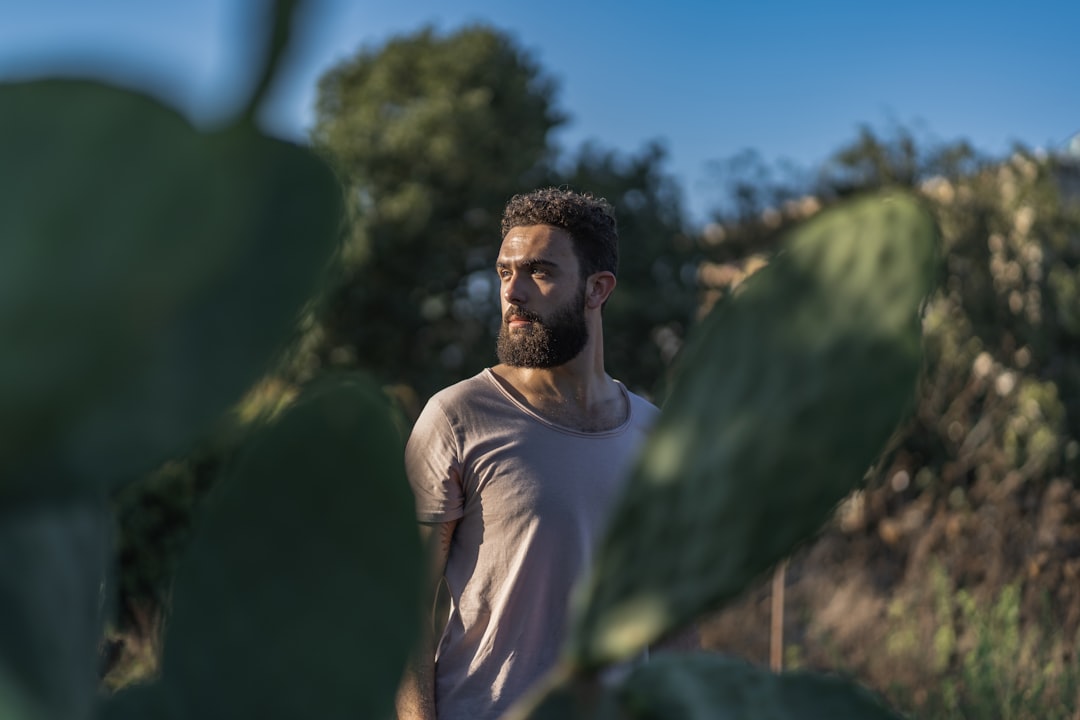 man in white crew neck t-shirt standing near green tree during daytime