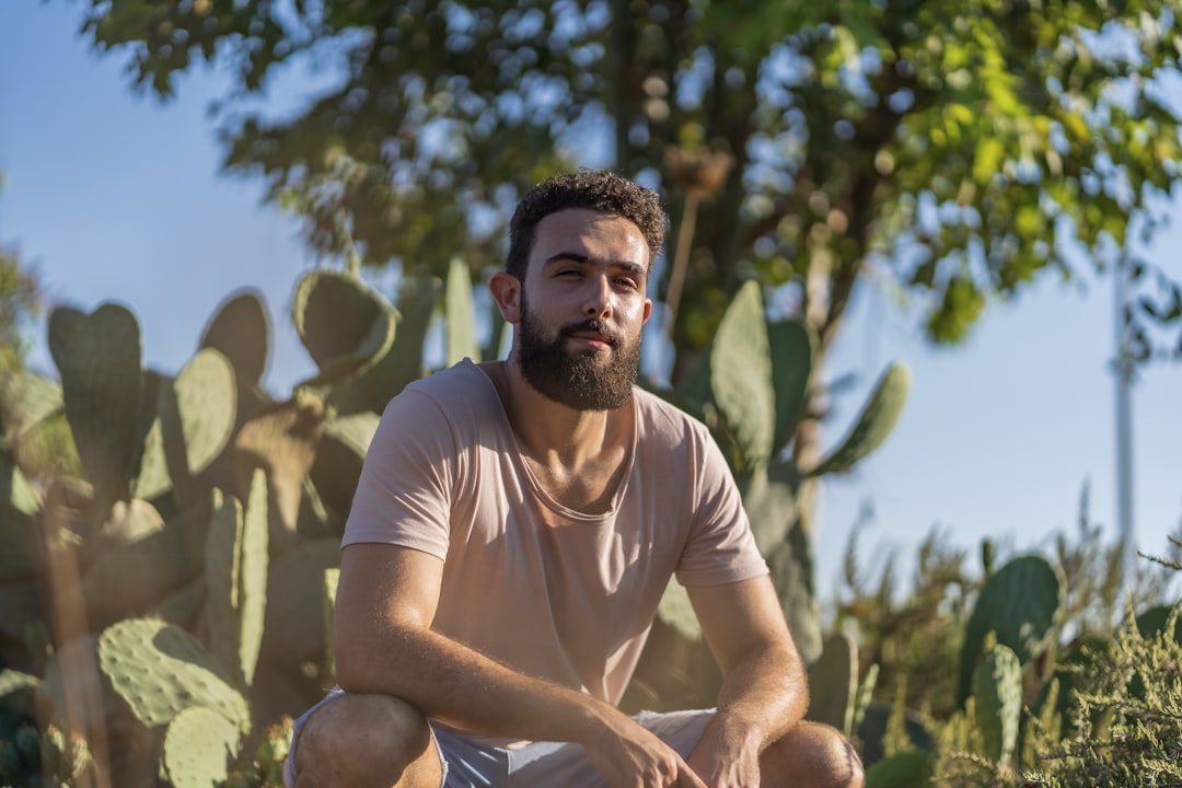 man in white crew neck t-shirt sitting on brown wooden chair during daytime