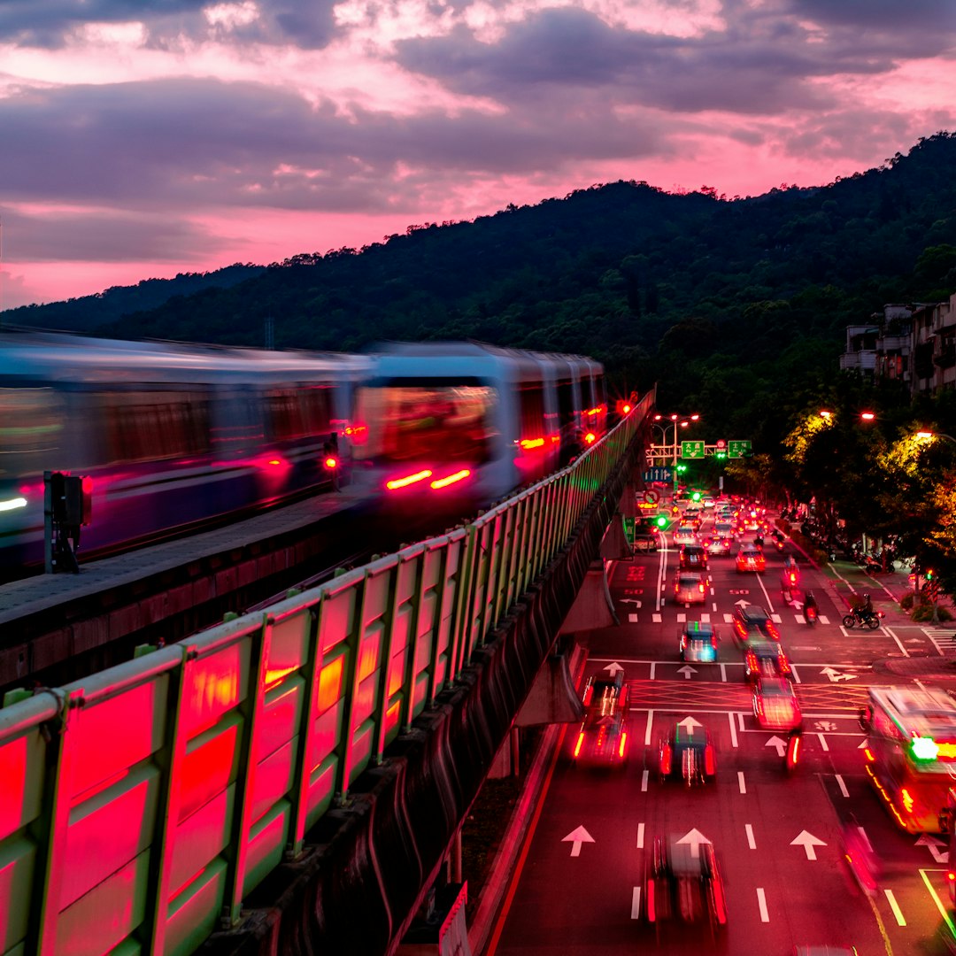 red and green train on rail near body of water during daytime