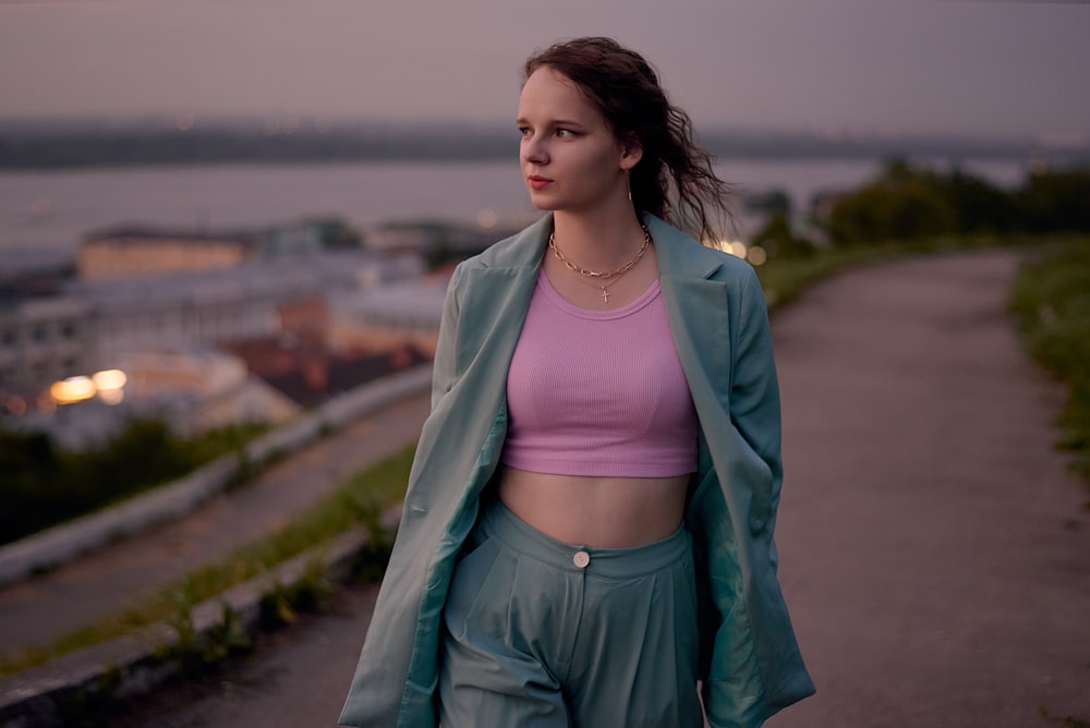 woman in pink crop top and green jacket standing on road during daytime