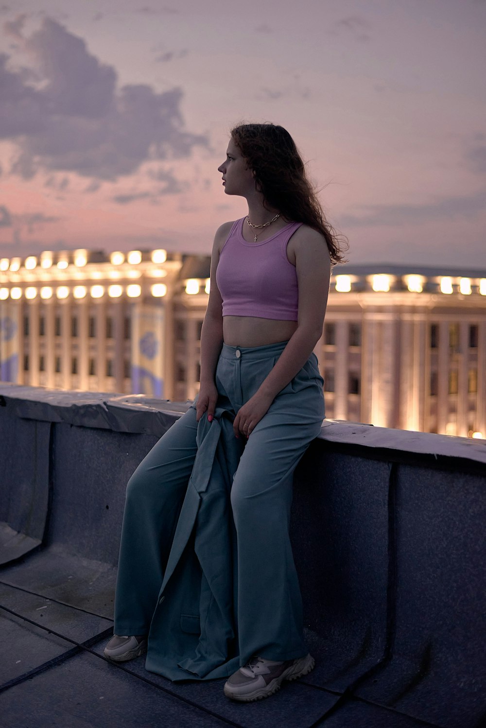 Donna in canotta bianca e jeans blu in denim che si siede su una panchina di cemento grigia durante il giorno