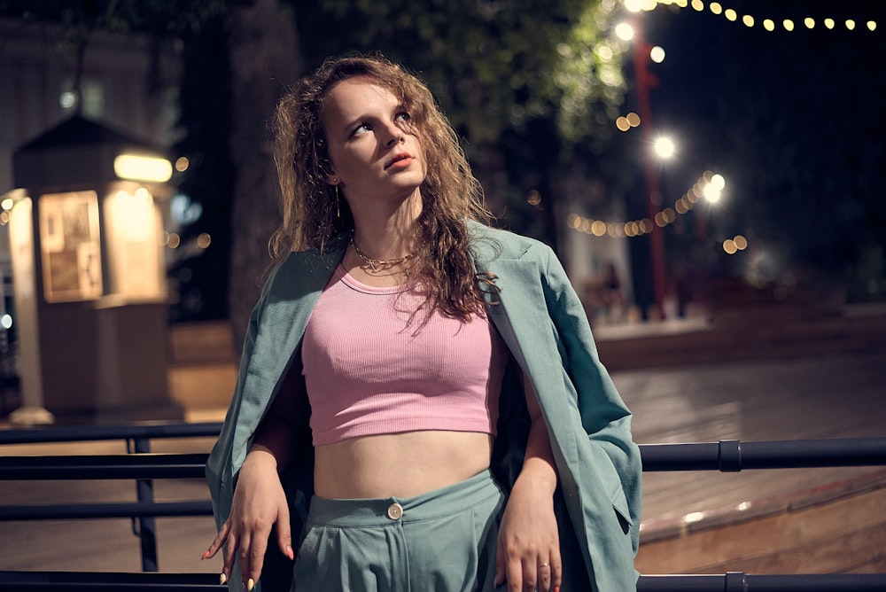 Frau in rosa Crop-Top und blauen Jeansshorts sitzt nachts auf brauner Holzbank