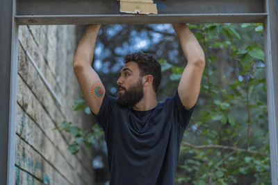 man in black crew neck t-shirt holding on grey metal bar