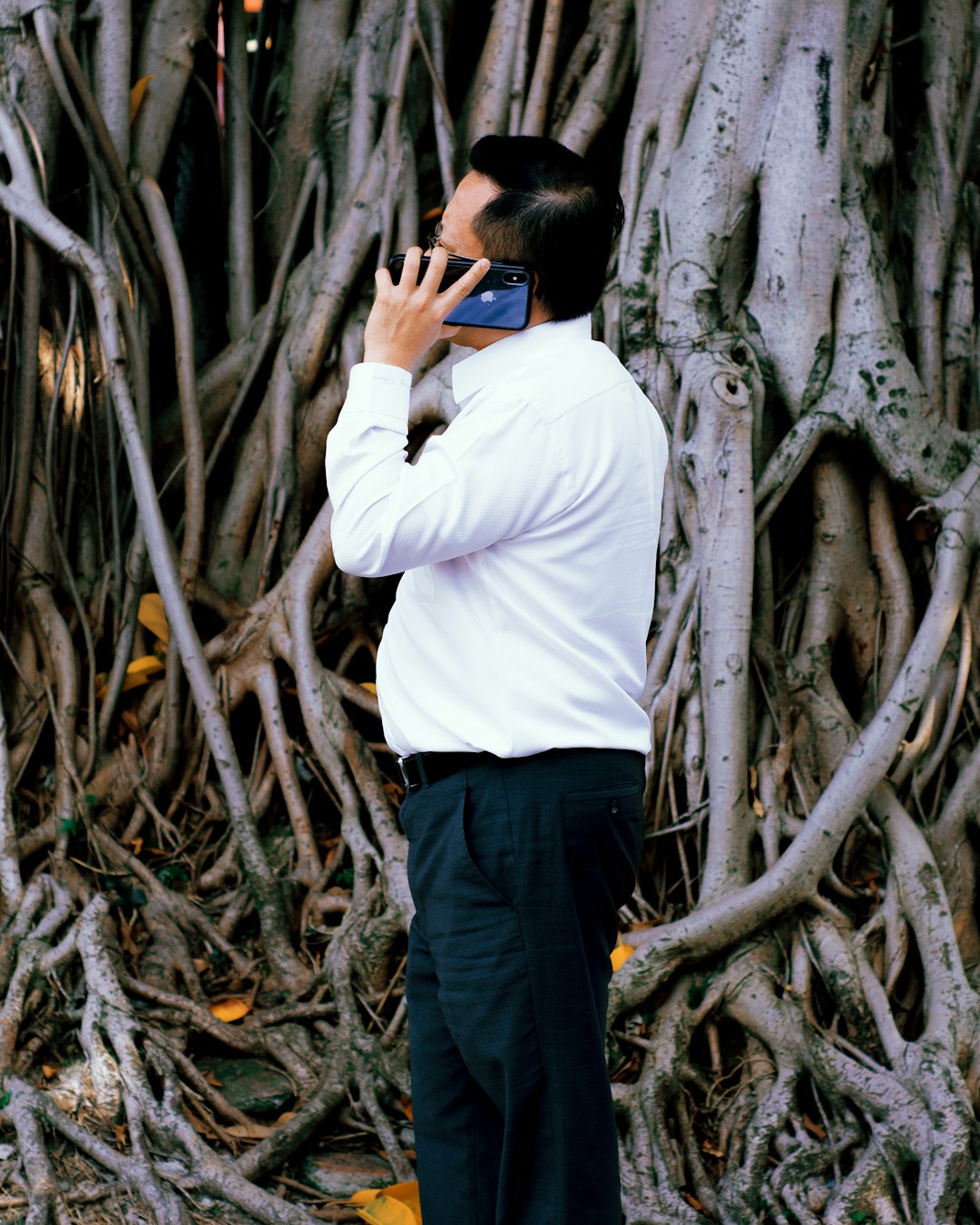 man in white dress shirt and black pants standing beside tree during daytime