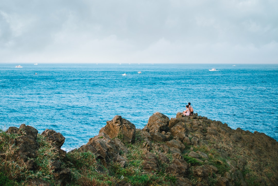 people sitting on rock formation near sea during daytime