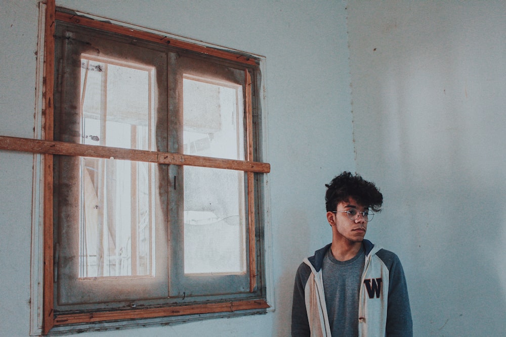 man in white and blue crew neck shirt standing near white wall