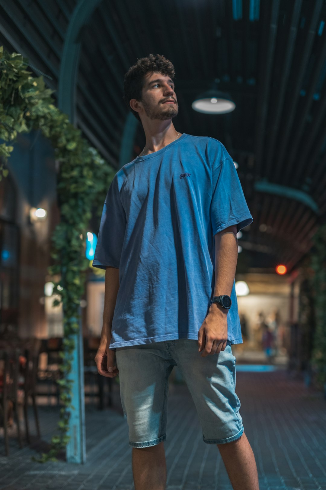 man in blue crew neck t-shirt and gray pants standing on sidewalk during nighttime