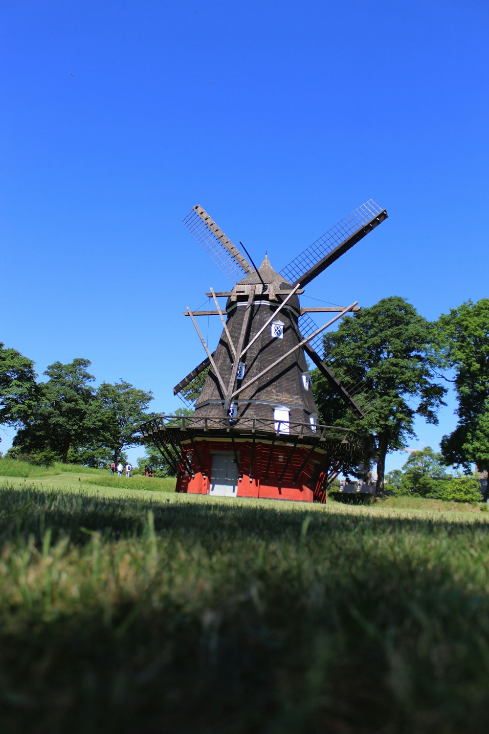 Molino de viento marrón y rojo en campo de hierba verde bajo cielo azul durante el día