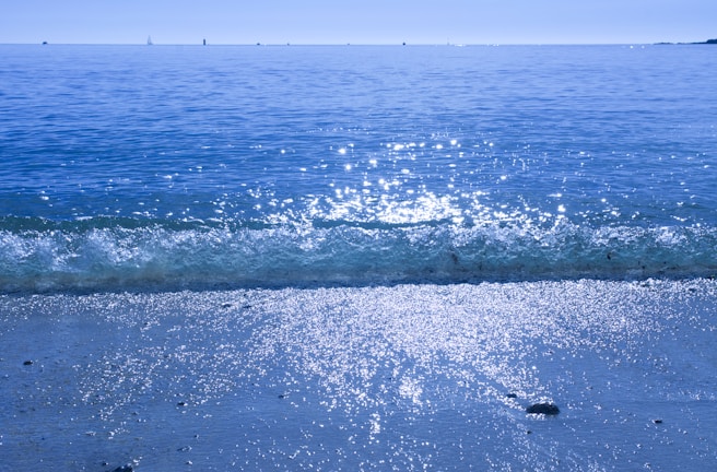 Sunlight sparkling on the calm ocean beside a sleek yacht under a clear blue sky.