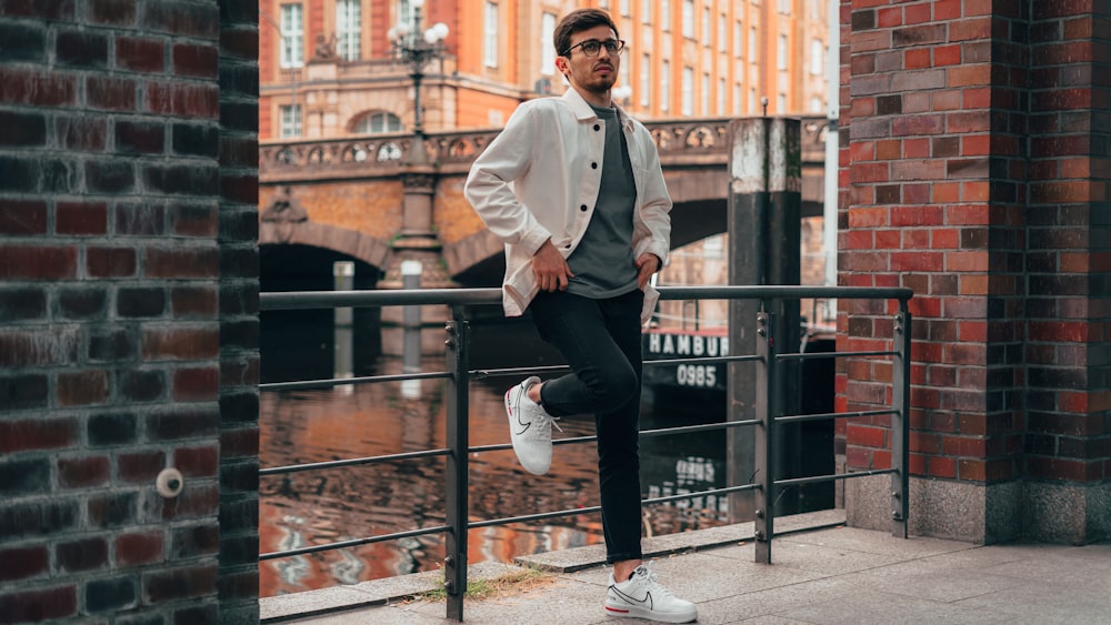 man in white dress shirt and black pants standing on black metal fence during daytime