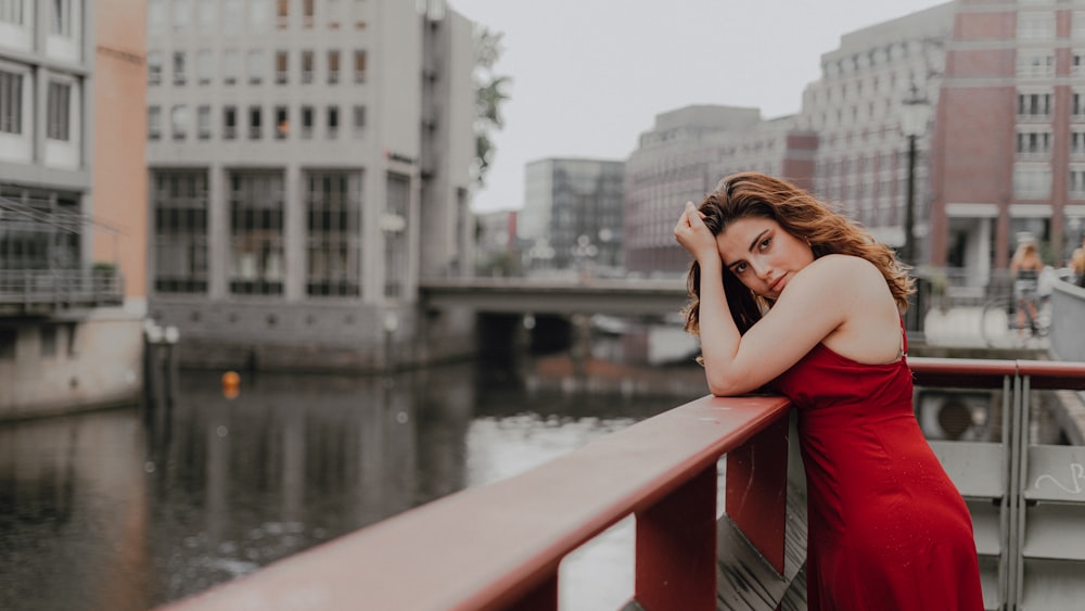 mulher no vestido vermelho sem mangas sentado no banco de madeira marrom perto do corpo de água durante o dia