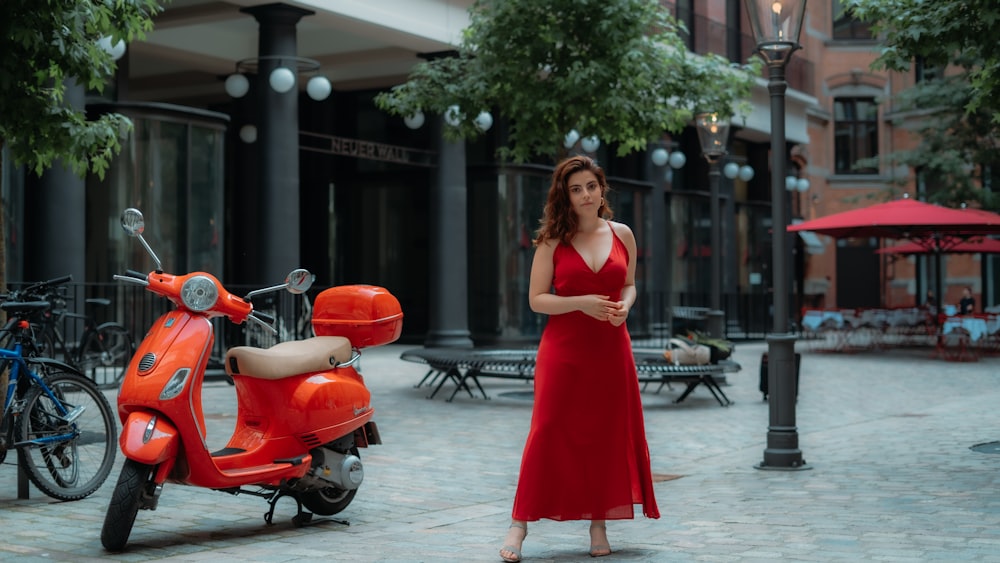 Frau in rotem ärmellosem Kleid steht tagsüber neben rotem Motorroller