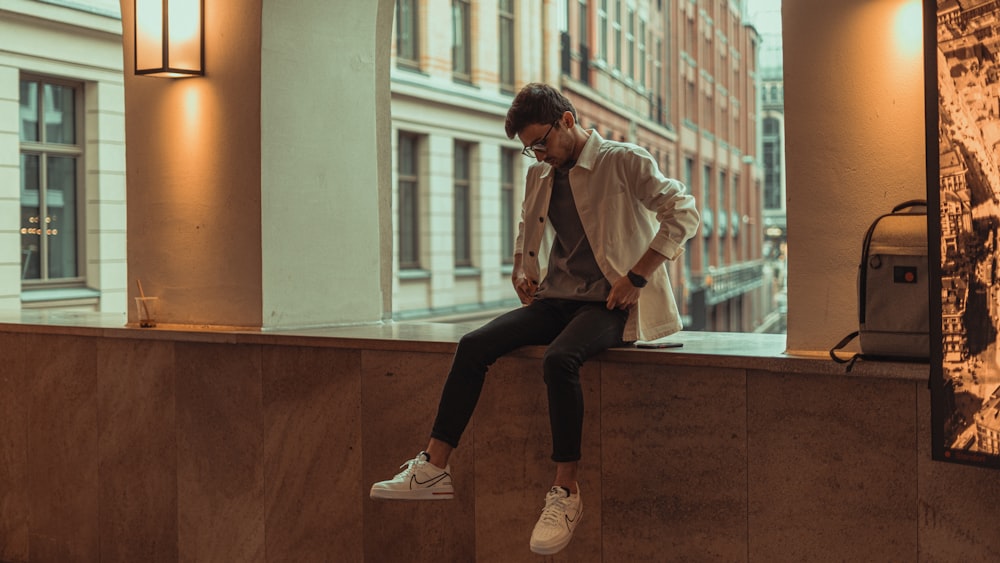 man in white dress shirt and black pants sitting on brown concrete wall during daytime