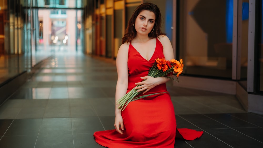 Femme en robe rouge à bretelles spaghetti tenant un bouquet de fleurs