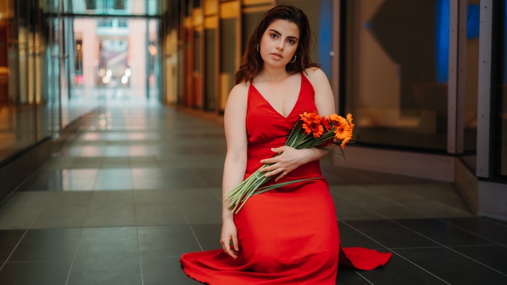 Mujer en vestido rojo de tirantes finos sosteniendo ramo de flores