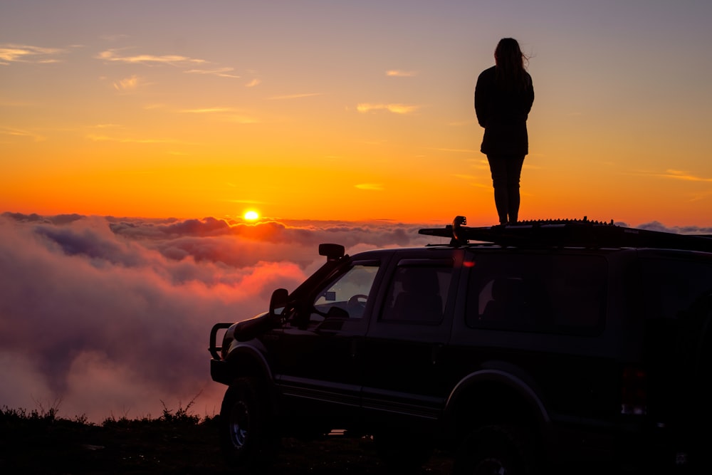 silhouette of man standing beside black suv during sunset