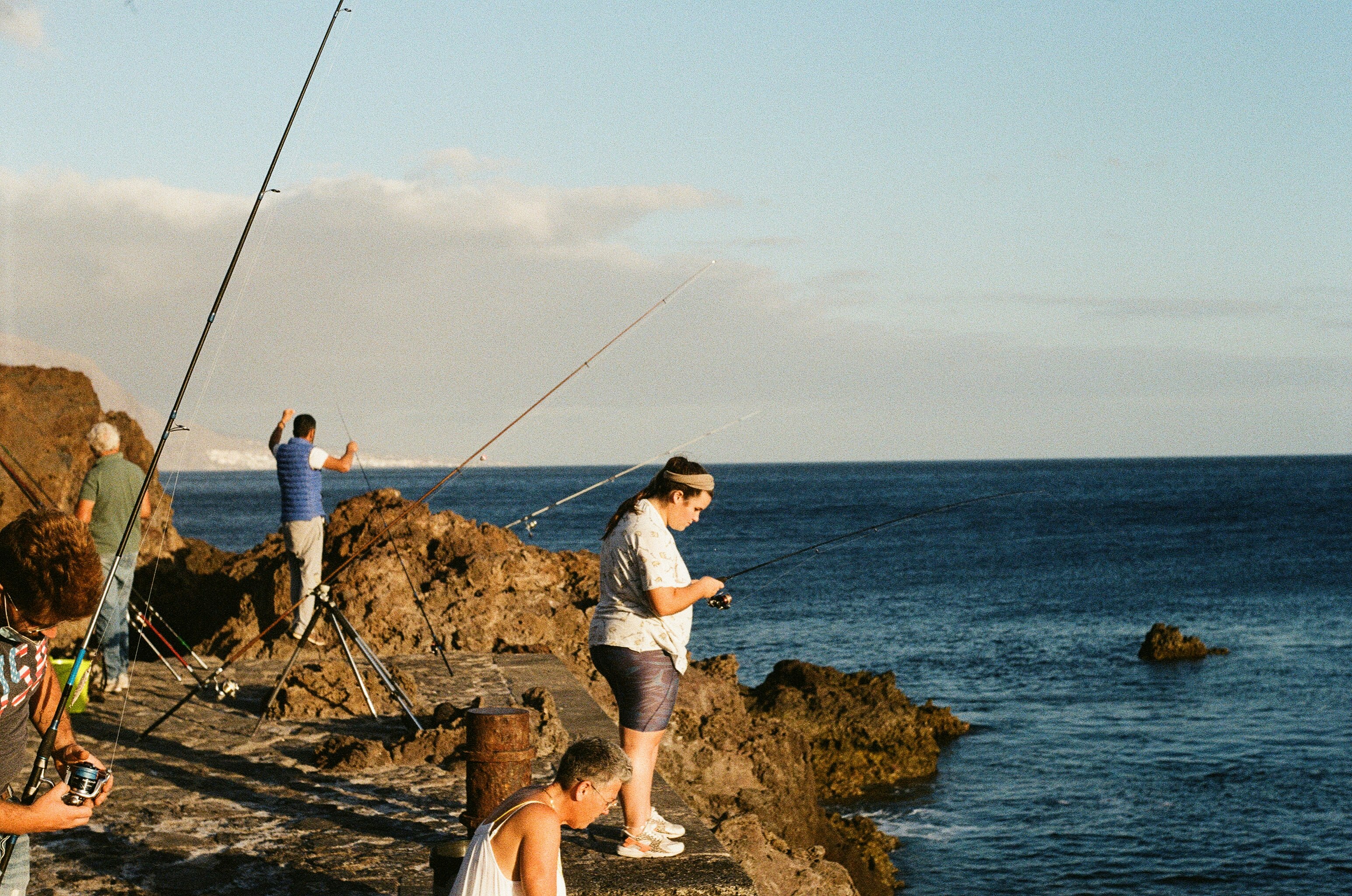 woman in white t-shirt and white shorts sitting on brown rock near body of water