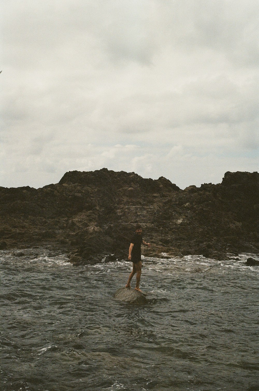 person in black shirt standing on gray rock formation in front of body of water during