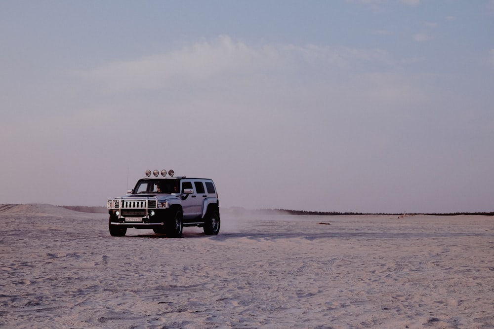 Jeep Wrangler blanco y negro sobre arena marrón bajo el cielo blanco durante el día