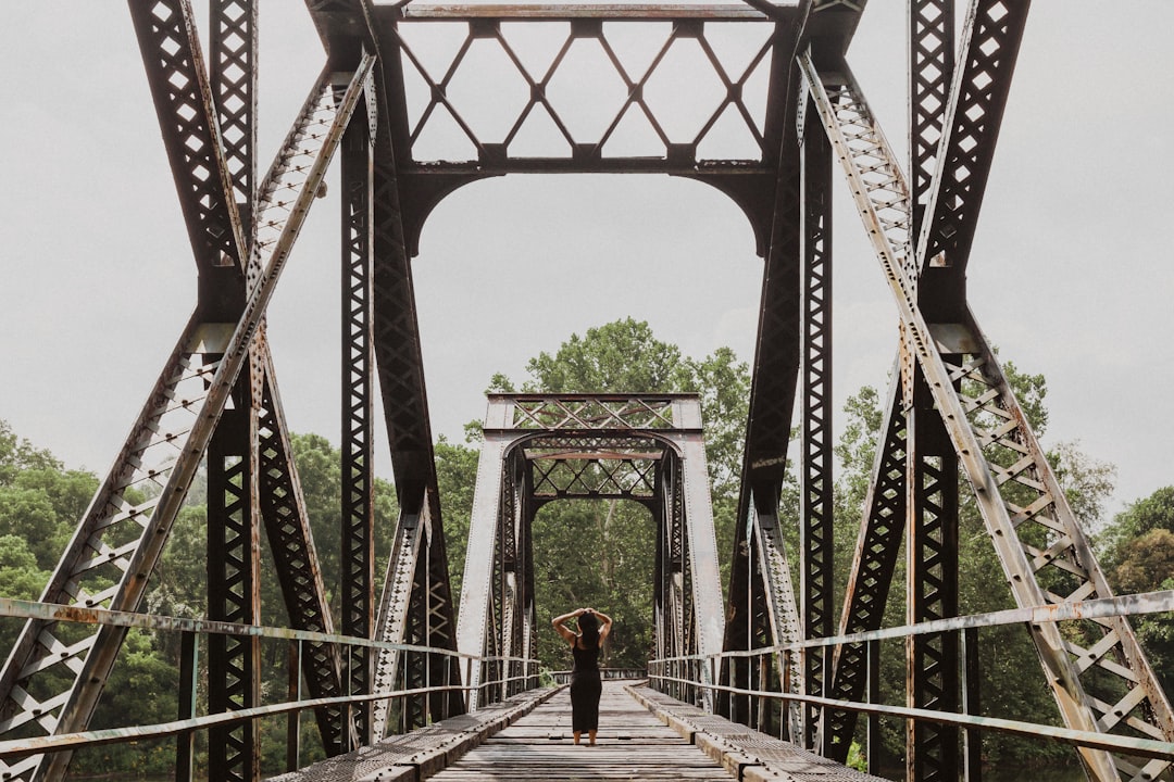 woman in black jacket and black pants walking on brown wooden bridge during daytime