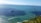 A large freight ship is sailing on a vast expanse of ocean under a clear blue sky. In the foreground, there are pieces of grass and plants, and in the distance, a landmass is visible on the horizon. Small waves can be seen on the water's surface.