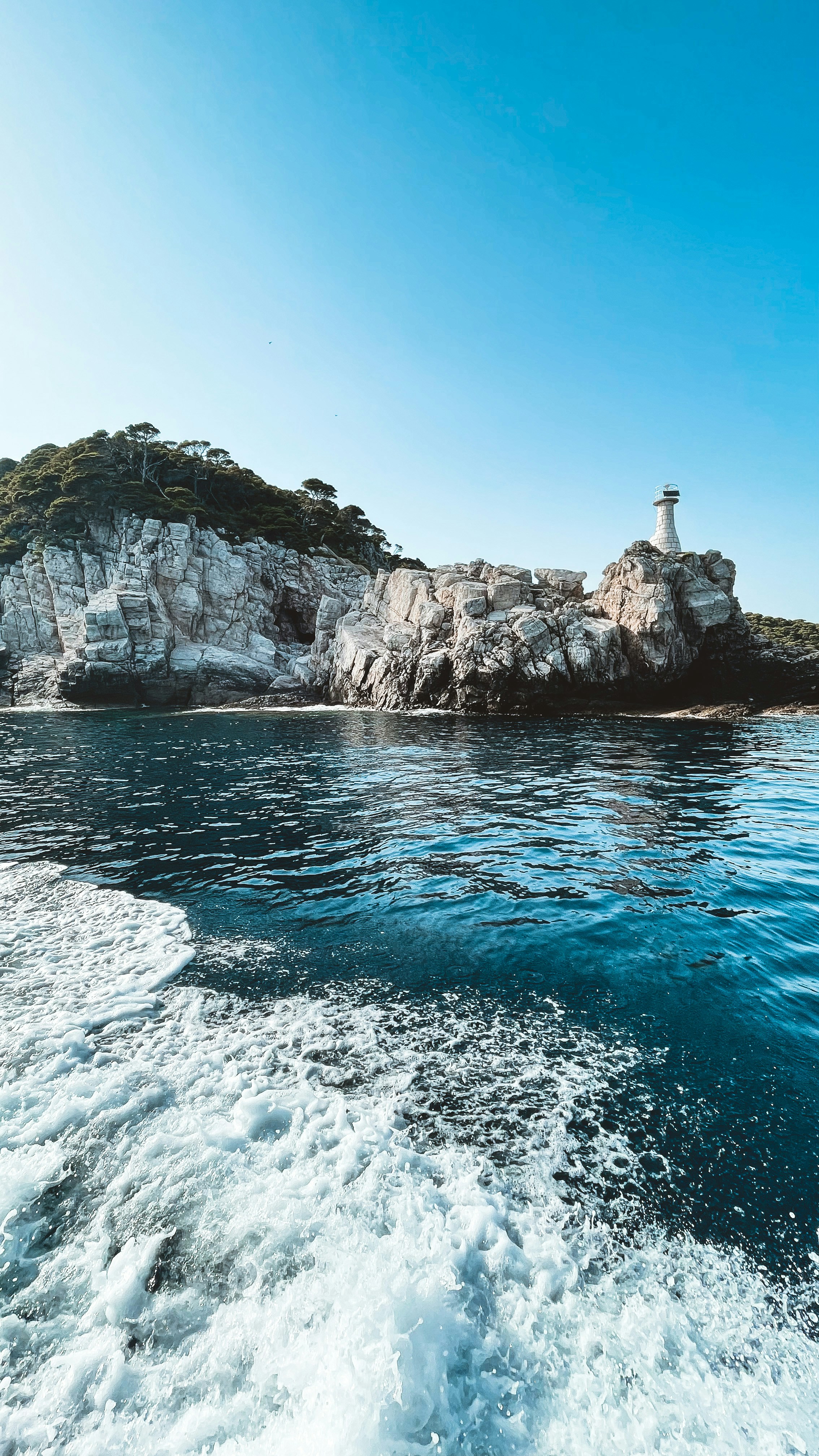 white and black lighthouse on rocky mountain beside sea during daytime