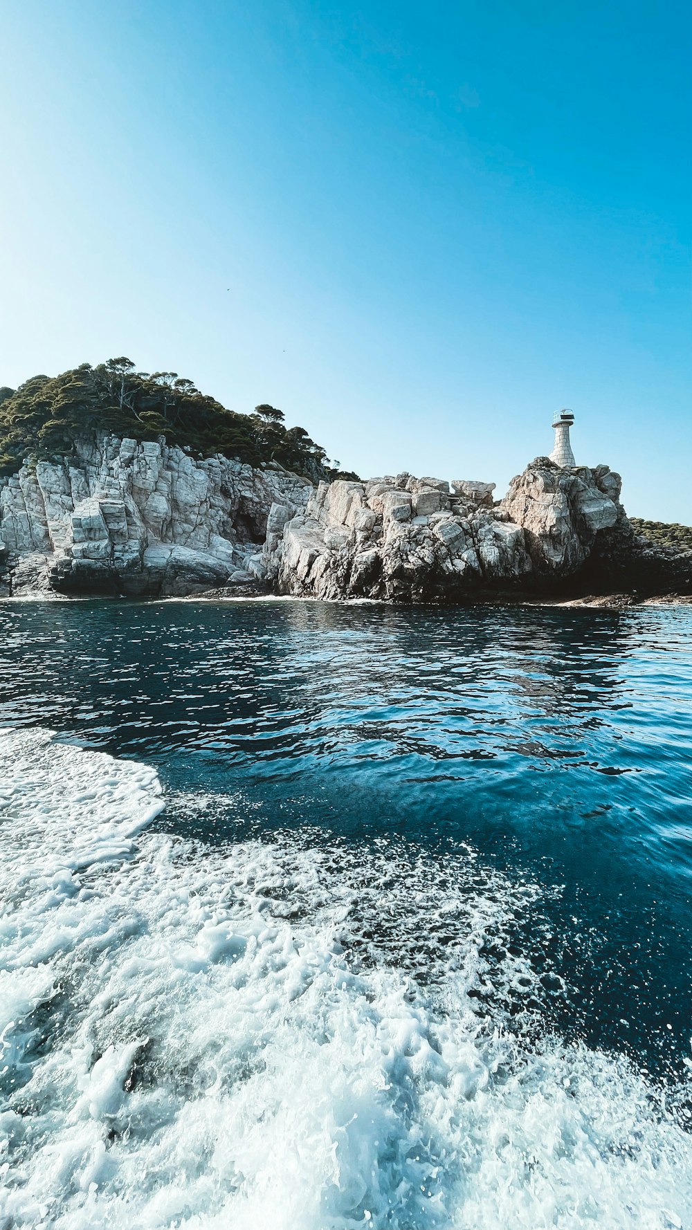 white and black lighthouse on rocky mountain beside sea during daytime