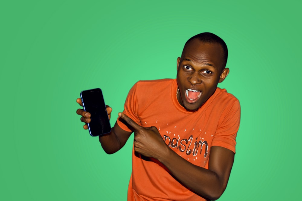 Hombre con camiseta naranja de cuello redondo sosteniendo un teléfono inteligente negro