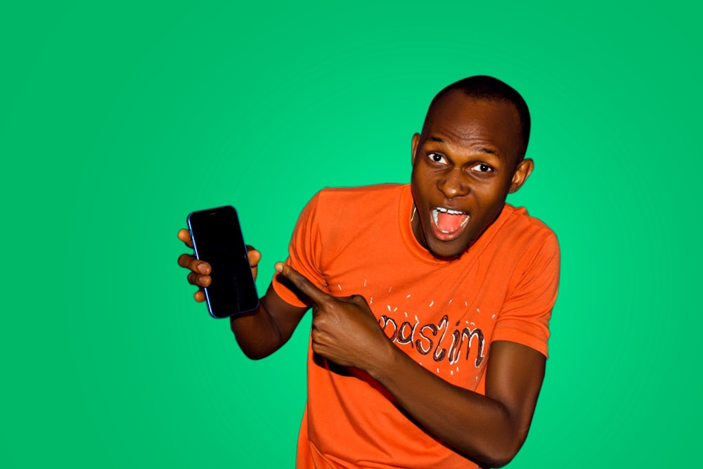 man in orange crew neck t-shirt holding black smartphone
